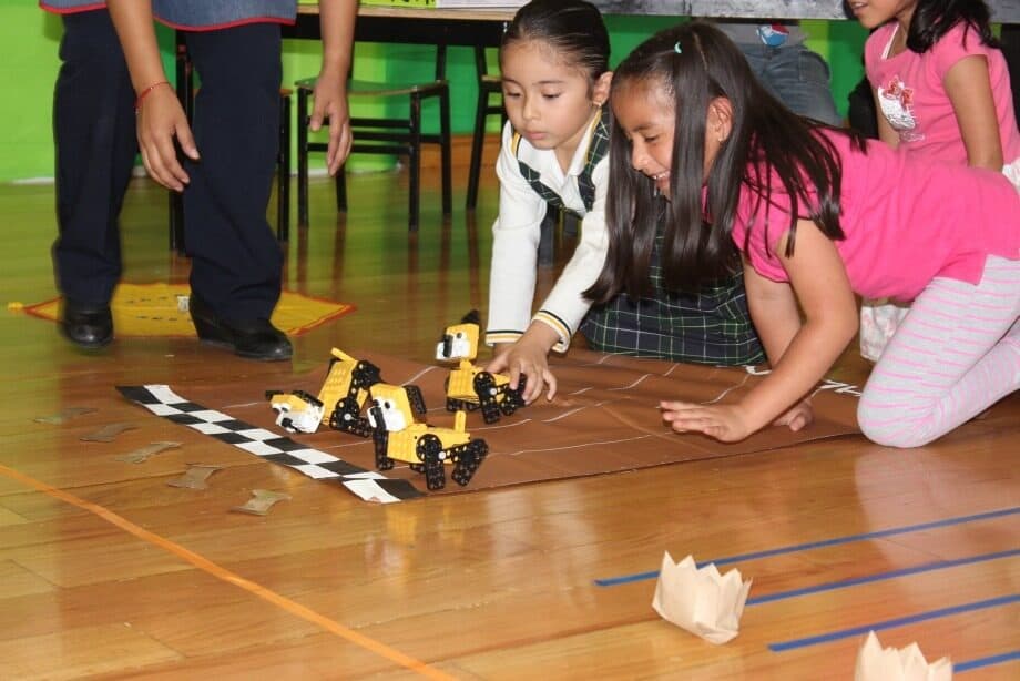 Dos alumnas guiando un carro robot amarillo sobre una pista de cuadros